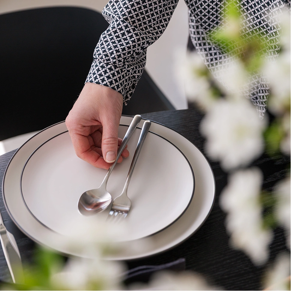 A hand places Calgary cutlery on a white plate with a black rim