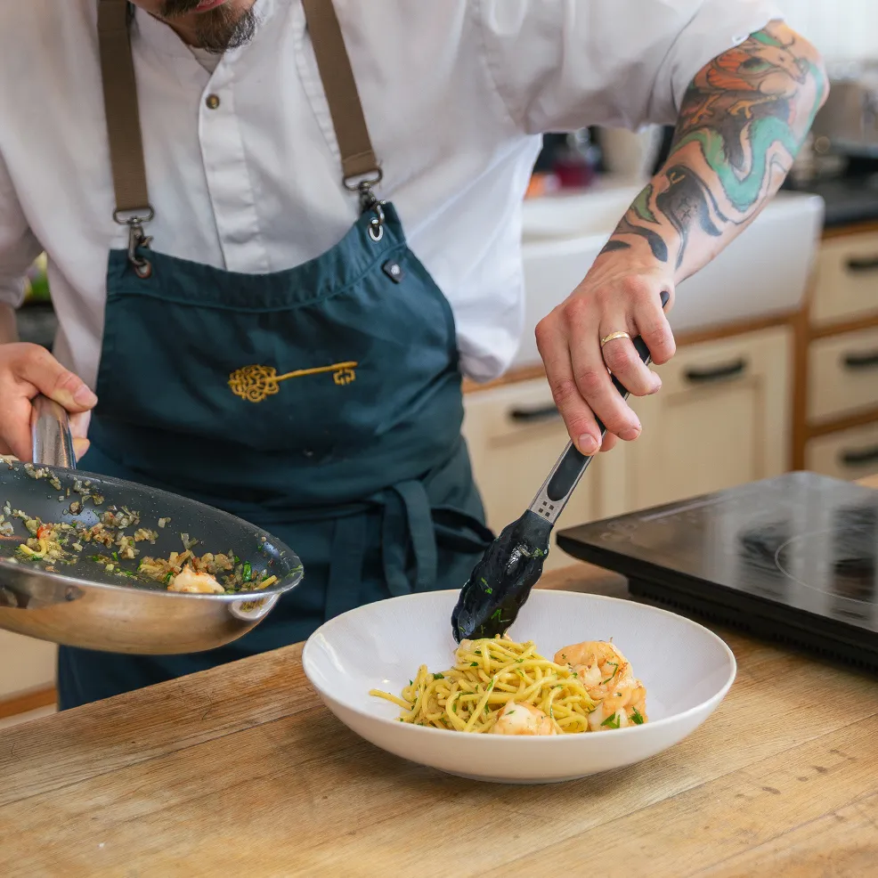 Ein Chefkoch vollendet Pasta in einer beigen Porzellanschüssel mit Küchenzangen 