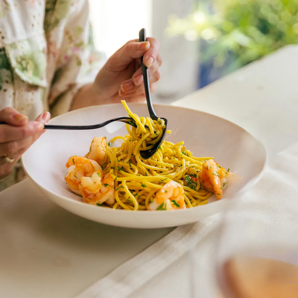 Spaghetti mit Garnelen in einer beigen Schüssel, aufgenommen mit Gabel und Löffel