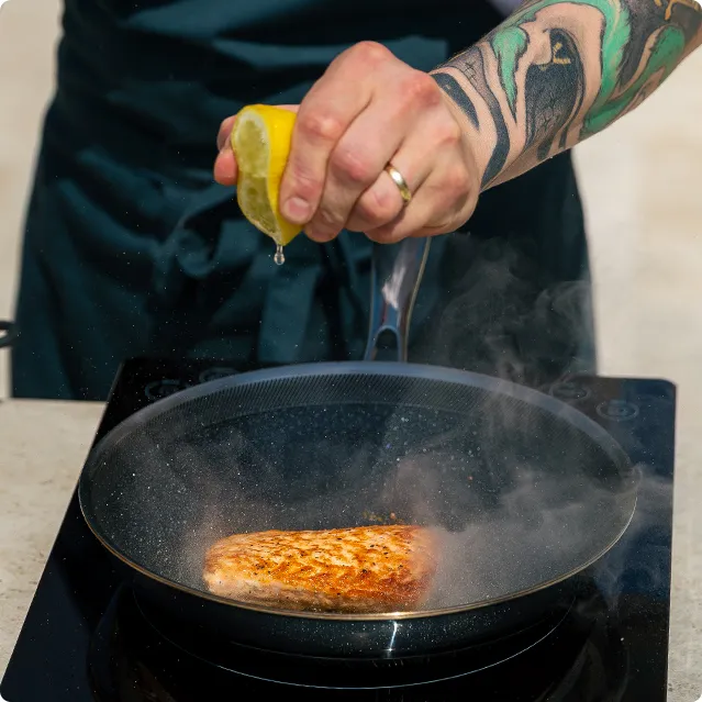 Detail einer Hand, die Zitrone in eine Pfanne mit zubereitetem Lachs ausdrückt