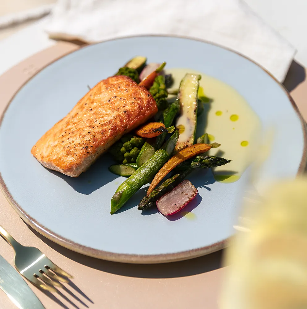 Lachs mit gegrilltem Gemüse, angerichtet auf einem hellblauen Teller